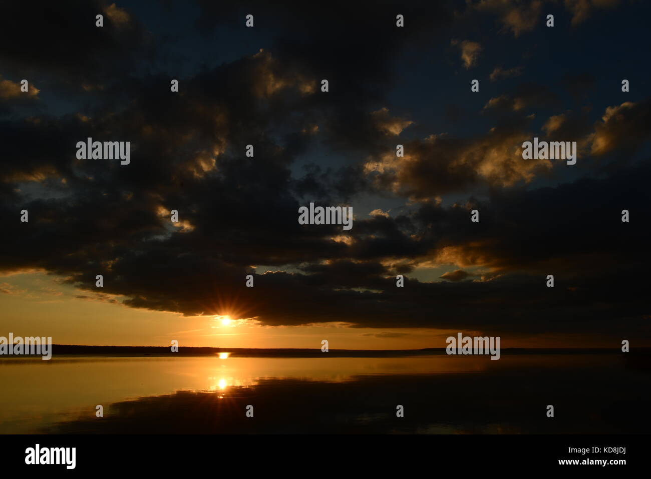 Il lago riflette il tramonto nel cielo di sunbeam circondato da il bagliore del sole sulla superficie dell'acqua sotto il cielo blu con nuvole Foto Stock