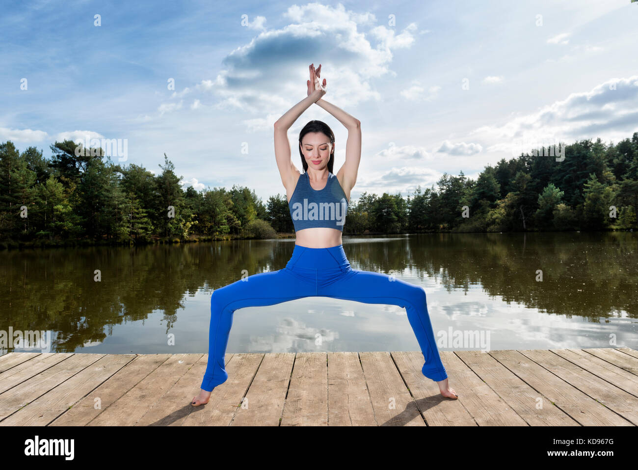 La donna a praticare yoga accanto a un lago, facendo la dea pongono. Foto Stock