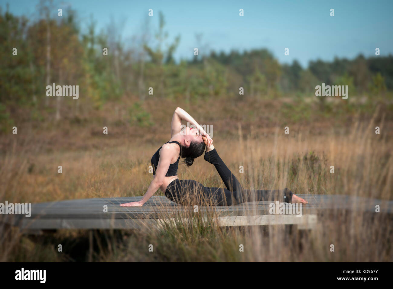 La donna a praticare yoga in campagna facendo una mezza prua, metà re cobra posa. Foto Stock