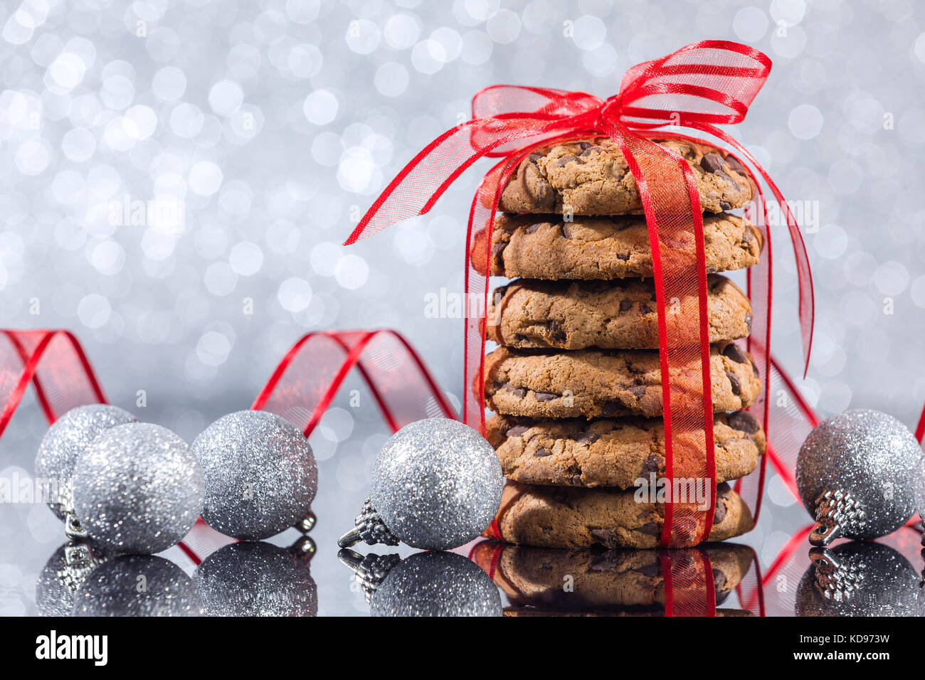 Pila di biscotti al cioccolato con decorazioni di Natale la riflessione sul tavolo di vetro su sfondo argento Foto Stock