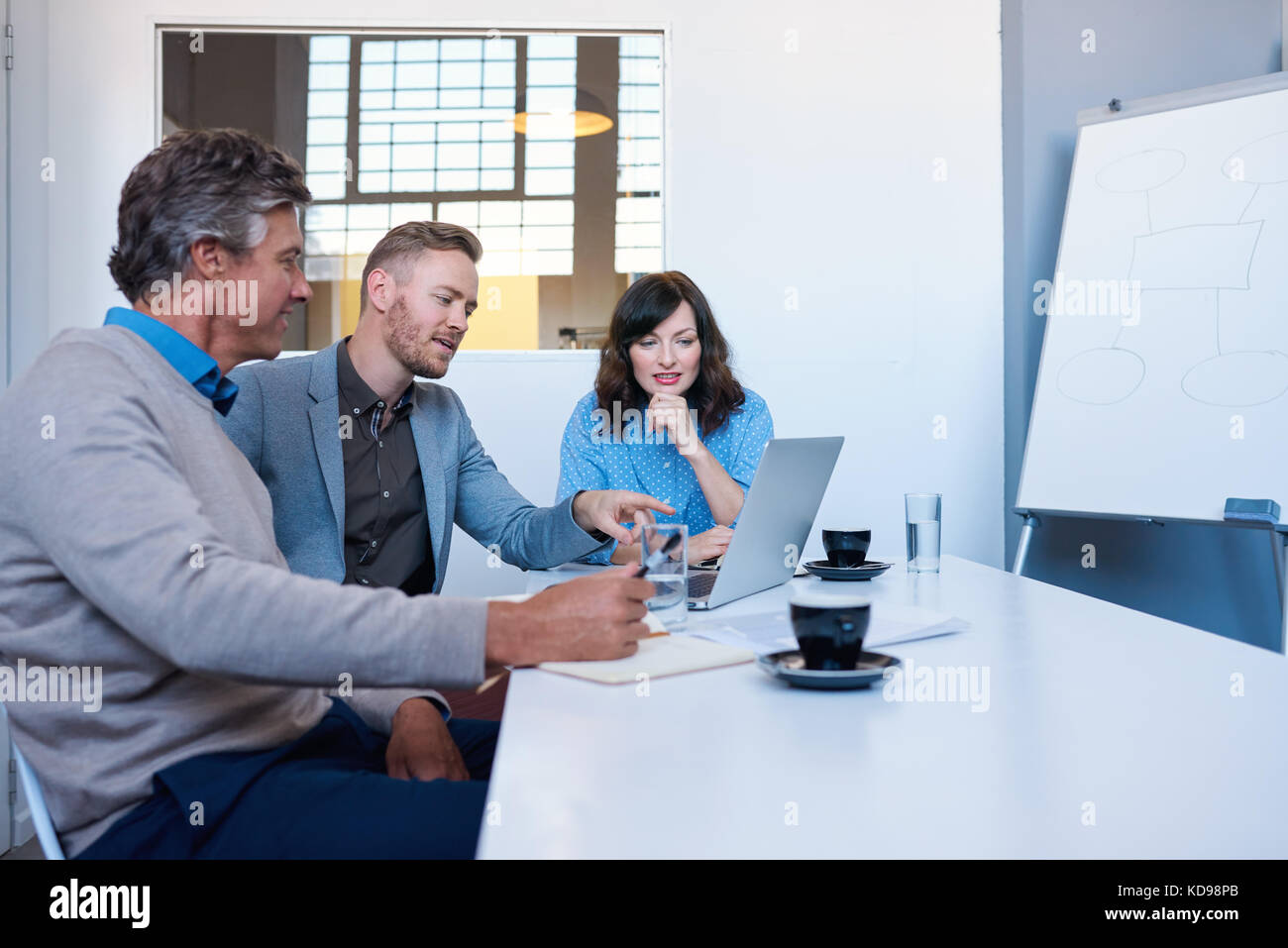 Tre imprenditori sorridente usando un computer portatile insieme in un ufficio Foto Stock