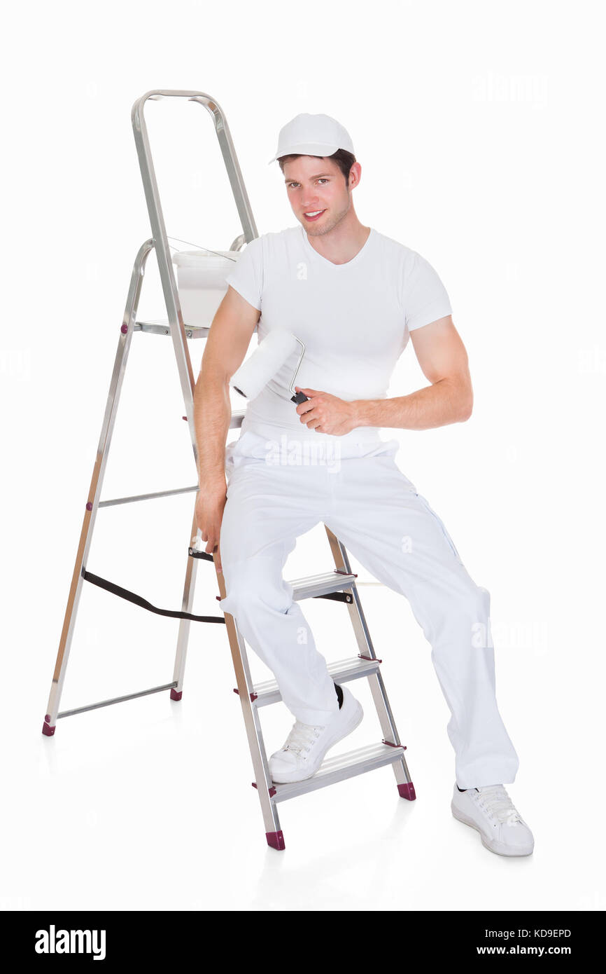Felice pittore con secchio di vernice e il rullo in piedi sulla scaletta Foto Stock