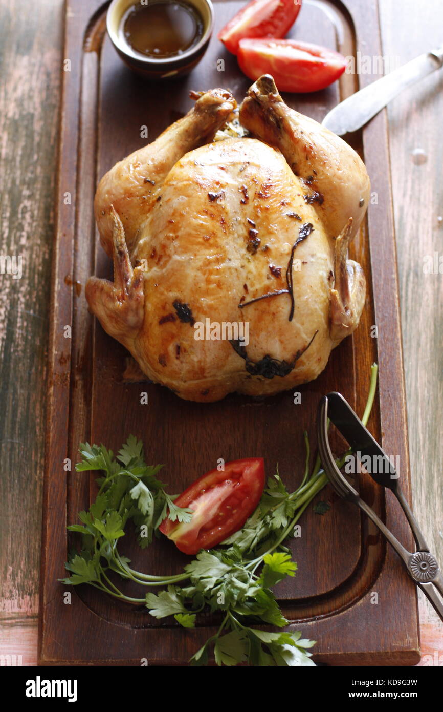 Rosted tutta la Turchia oltre il buio tagliere di legno con pomodoro, erbe aromatiche e una ciotola di salsa gravy Foto Stock