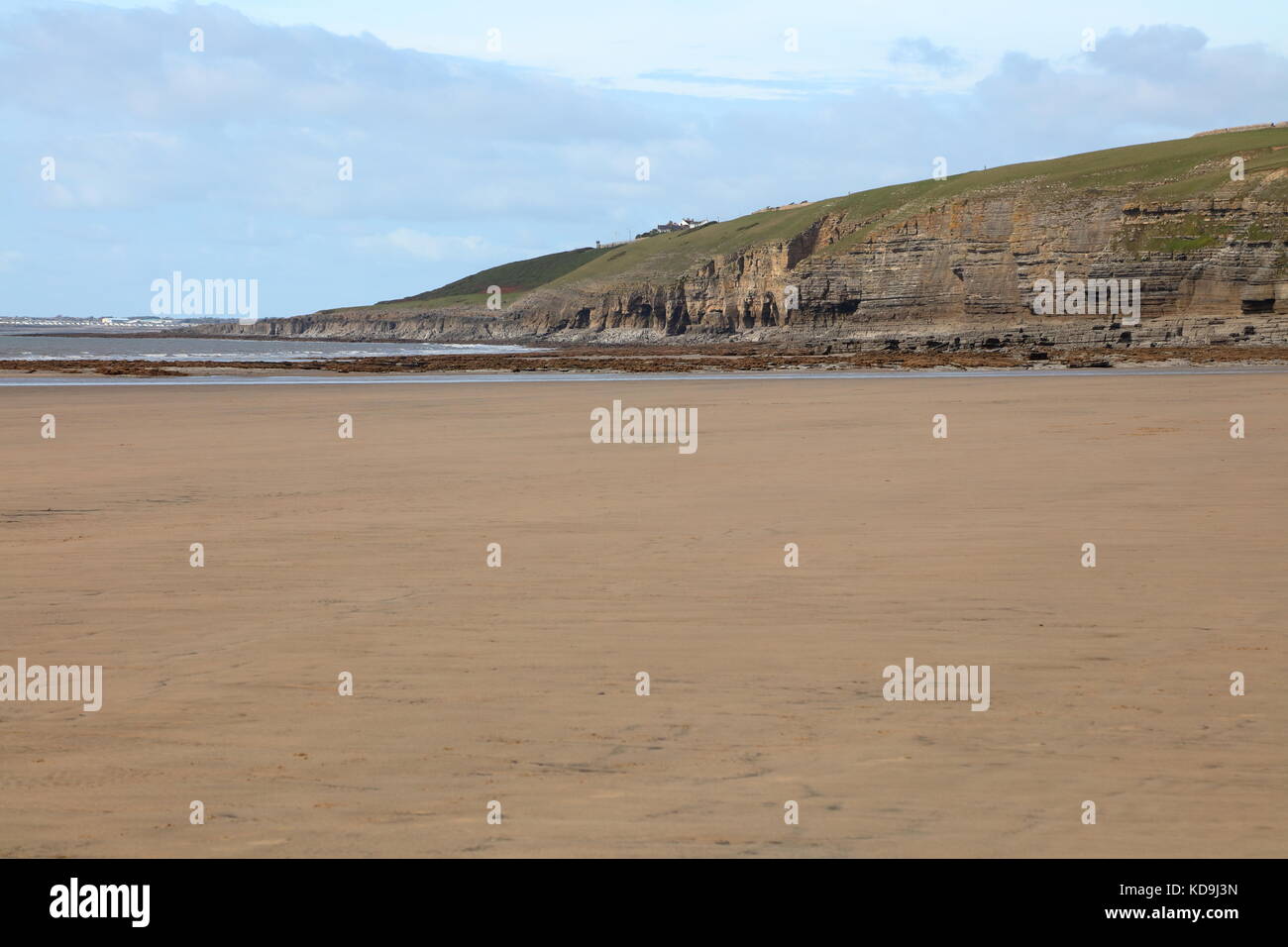 Dunraven baia con una bassa marea che mostra vaste distese di spiaggia di sabbia con la roccia pile a distanza al di sotto delle enormi scogliere di roack instabile. Foto Stock
