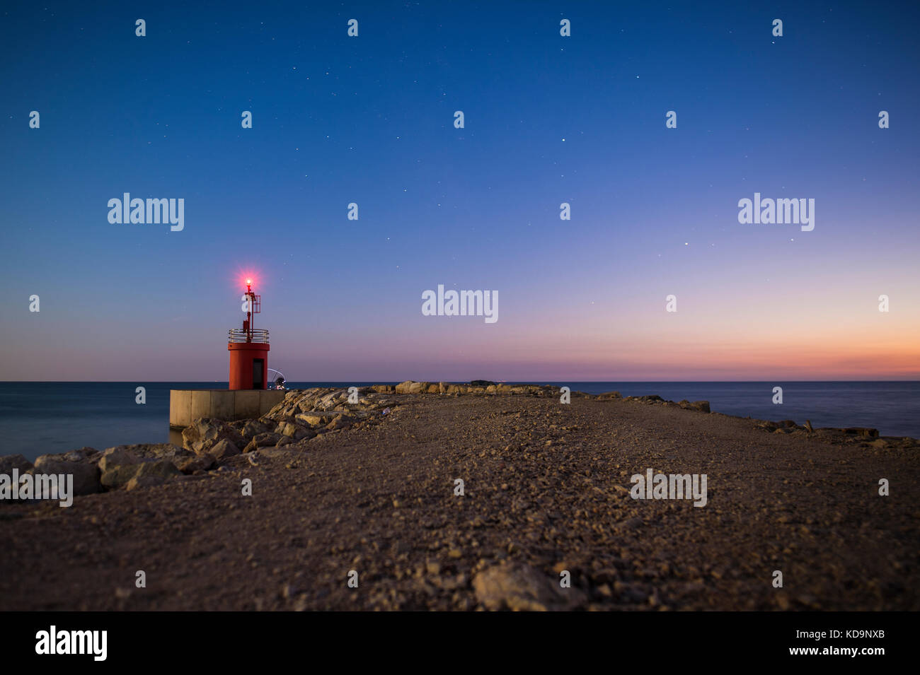 Seascape di una sostanziosa strada che conduce ad un piccolo faro illuminato. Foto scattata al tramonto nella spiaggia di Sabaudia, Italia. Foto Stock