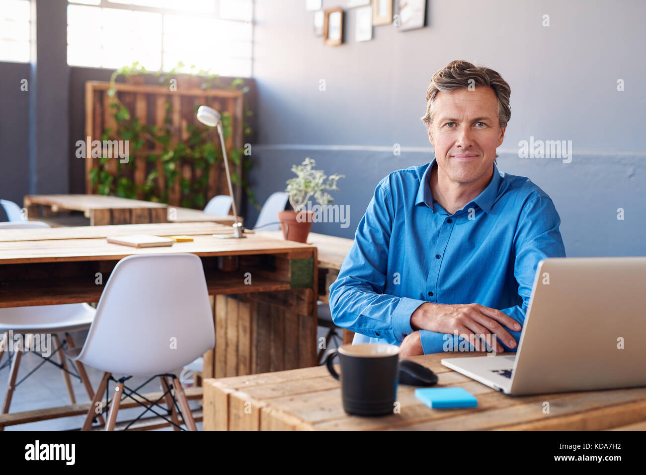 Sorridente imprenditore maturo seduto alla sua scrivania in un ufficio Foto Stock