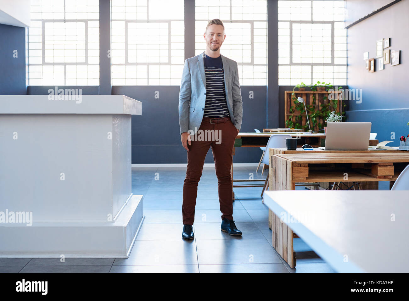Sorridente giovane imprenditore in piedi da solo in un ufficio moderno Foto Stock