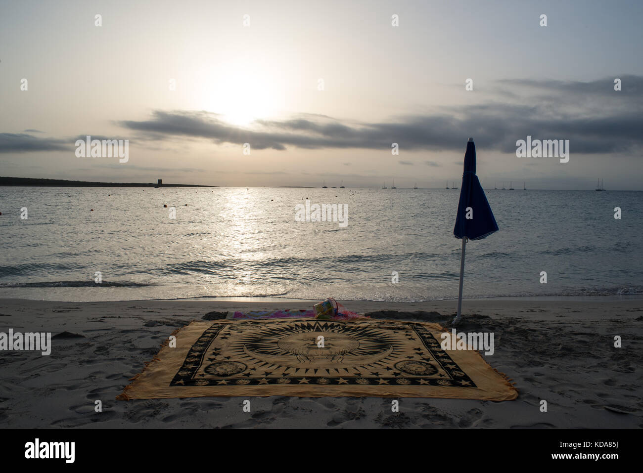 Una vista panoramica della spiaggia della Pelosa presso sunrise in estate. un telo da spiaggia e ombrellone in spiaggia con mare in background. Foto Stock
