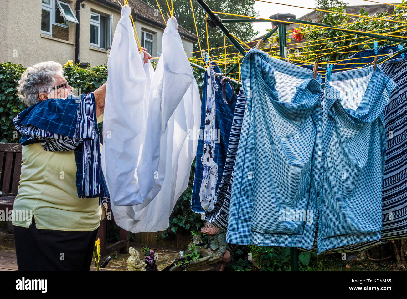 Un vecchio / anziani / senior lady (età 80) appeso fuori lavaggio wet nel suo giardino, in un giorno caldo, inizio autunno. South Ealing, West London W5, Inghilterra, Regno Unito. Foto Stock