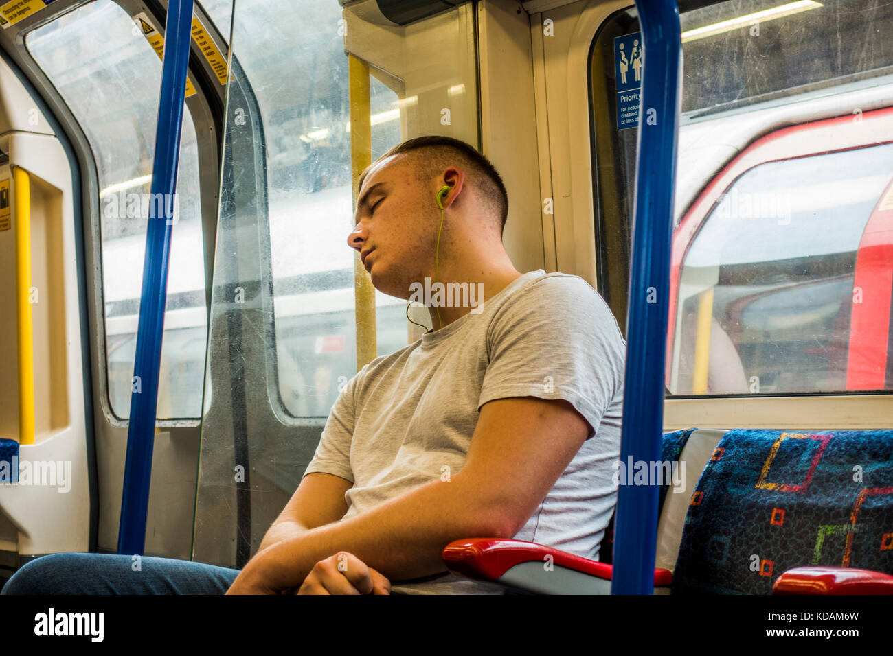 La metropolitana di Londra treno tubo - giovane uomo addormentato, indossando le cuffie su un tranquillo viaggio diurno con nessun altro i passeggeri a bordo del carrello. Inghilterra, Regno Unito. Foto Stock