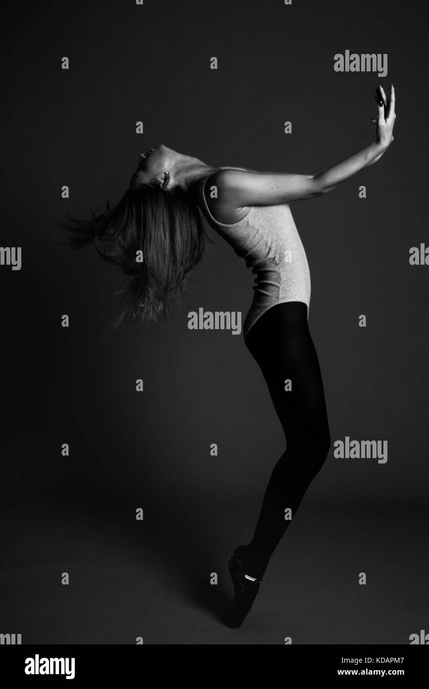 Giovane donna bellissima ballerina con lunghi capelli neri indossando giubbotto grigio e collant saltando su un grigio chiaro di sfondo per studio Foto Stock