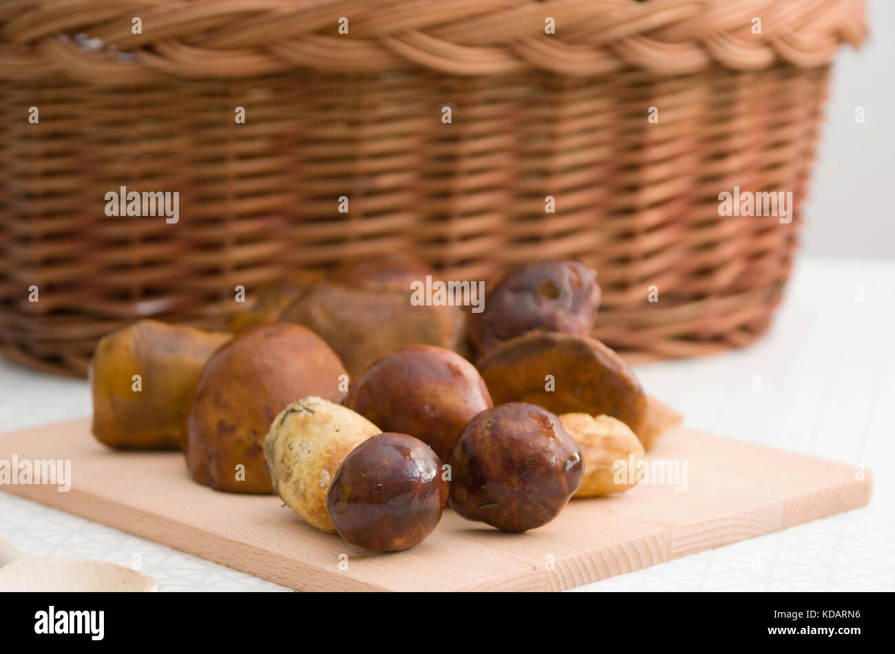 Cesto pieno di funghi in piedi sulla tavola e funghi su un pannello preparato per il taglio. Foto Stock