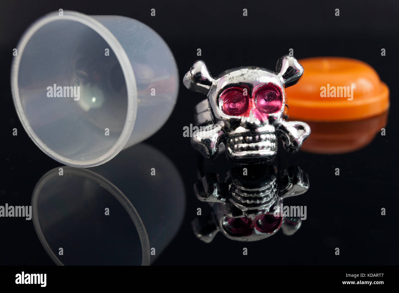Close up del giocattolo di plastica cranio argento e anello crossbones su sfondo nero. gumball machine premio. Foto Stock