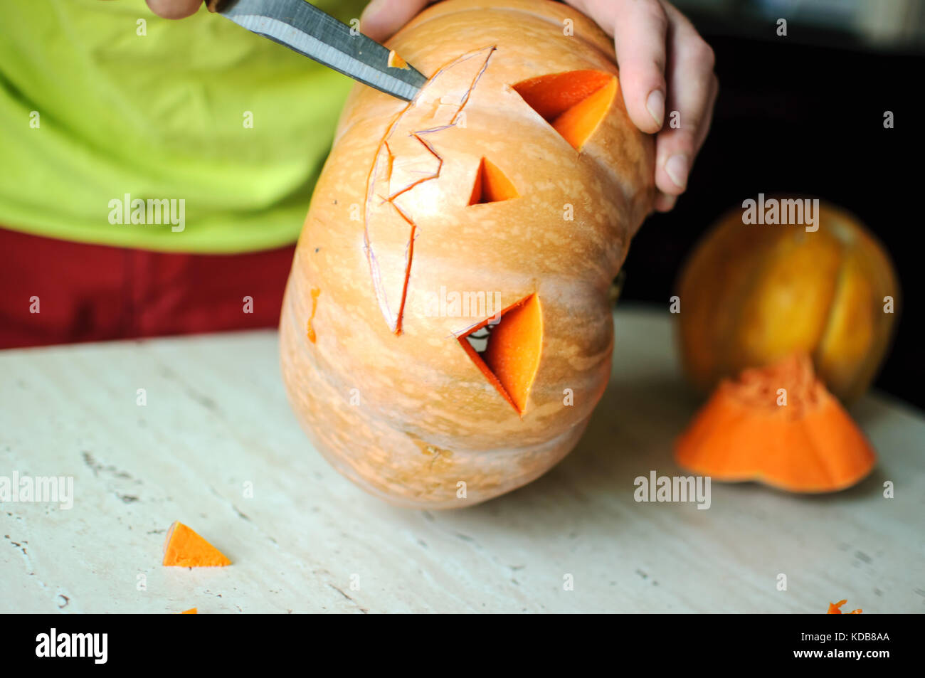 Zucca di Halloween processo di taglio, il processo di realizzazione di jack-o-lantern maschio mani con coltello, gli avanzi di zucca sul tavolo della cucina. messa a fuoco selettiva Foto Stock