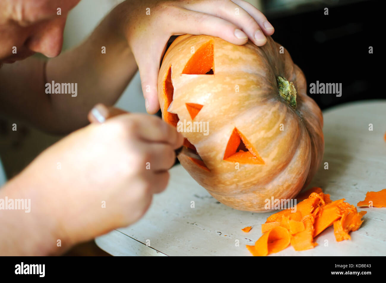 Zucca di Halloween processo di taglio, il processo di realizzazione di jack-o-lantern maschio mani con coltello, gli avanzi di zucca sul tavolo della cucina. messa a fuoco selettiva Foto Stock