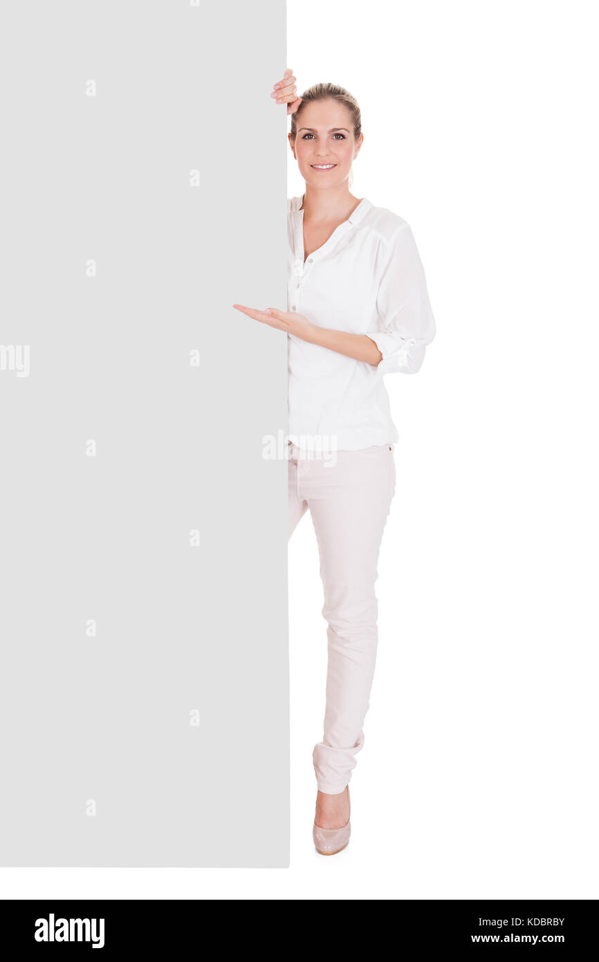 Giovane donna in piedi vicino alla targhetta vuota e presentante su sfondo bianco Foto Stock