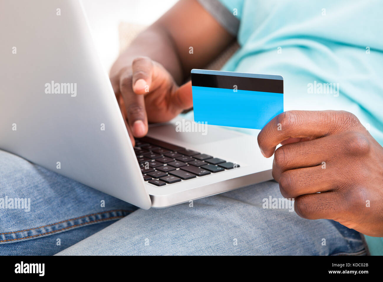 Felice del giovane africano utilizzando laptop seduto sul divano di casa Foto Stock