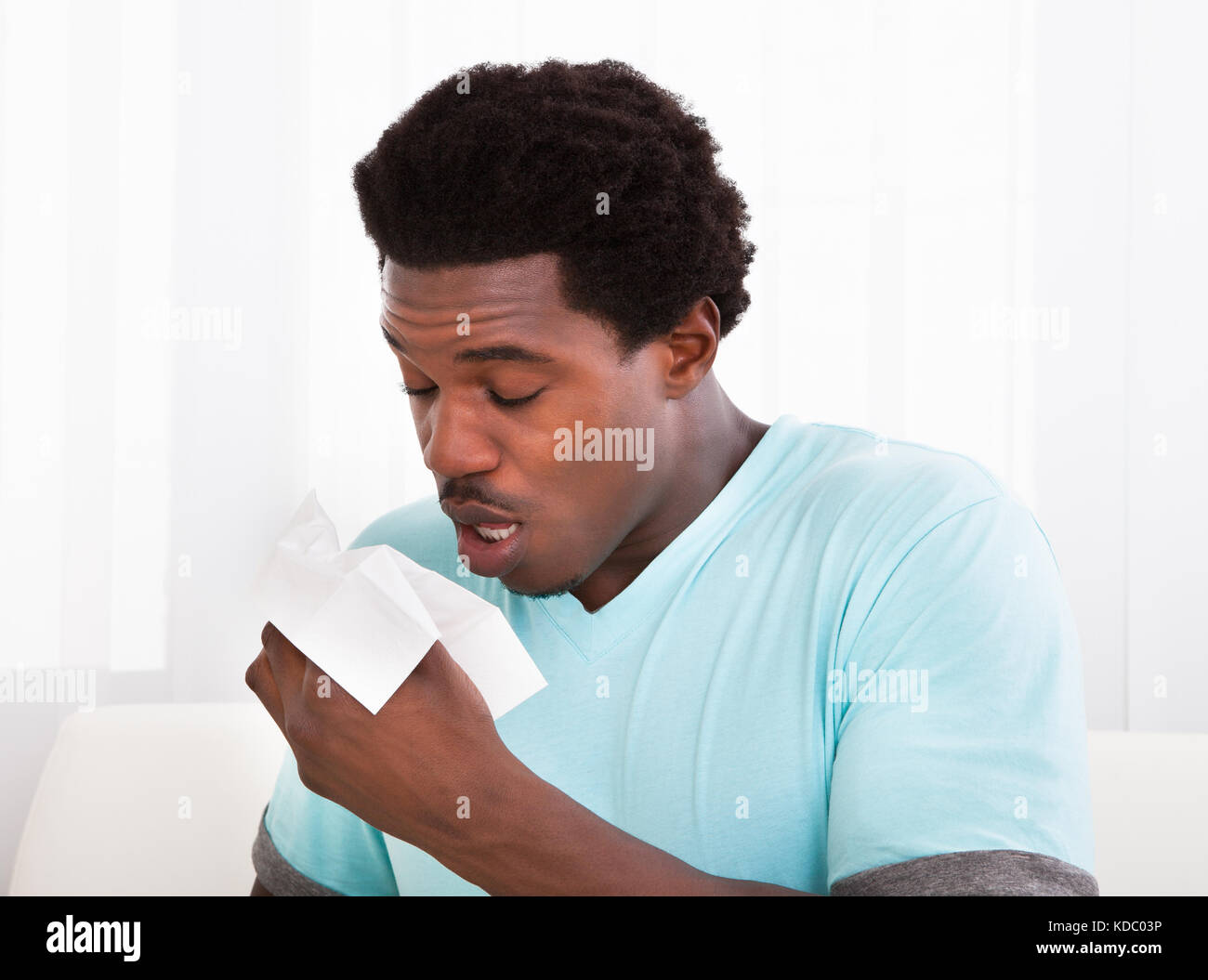 African giovane uomo avente un freddo il trattenimento del tessuto e soffiare il naso Foto Stock