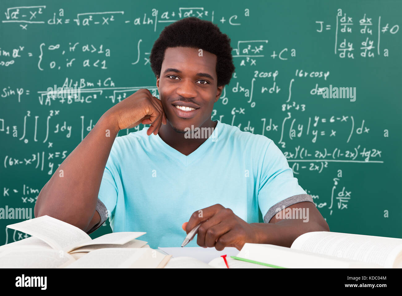 Giovane africano a studiare con un sacco di libri di seduta di fronte di Blackboard Foto Stock