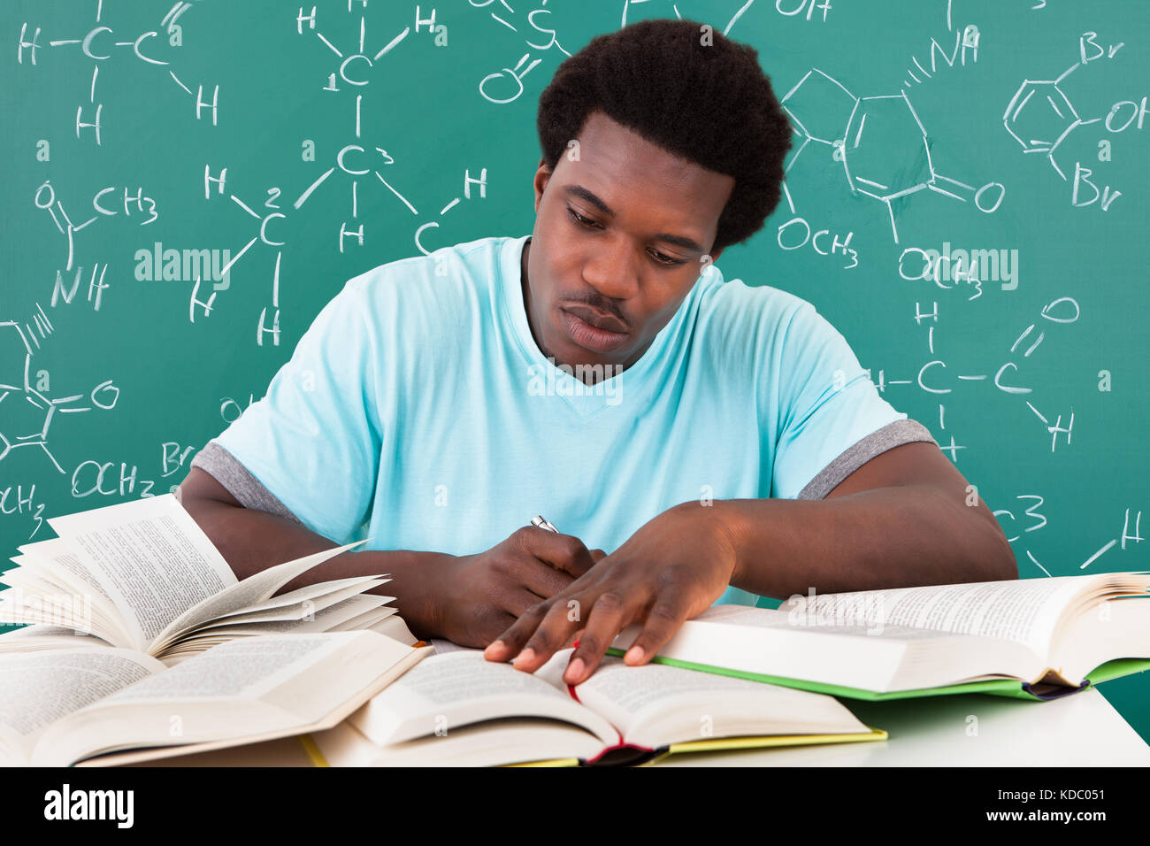 Giovane africano a studiare con un sacco di libri di seduta di fronte di Blackboard Foto Stock