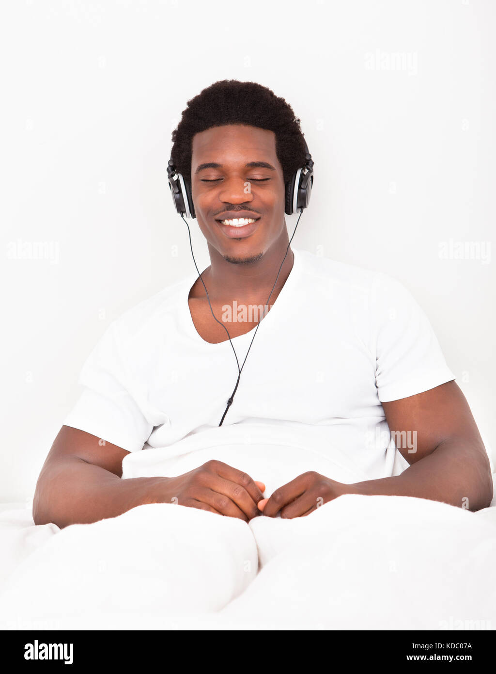 Felice rilassata del giovane africano seduta sul letto ascoltando musica in cuffia Foto Stock