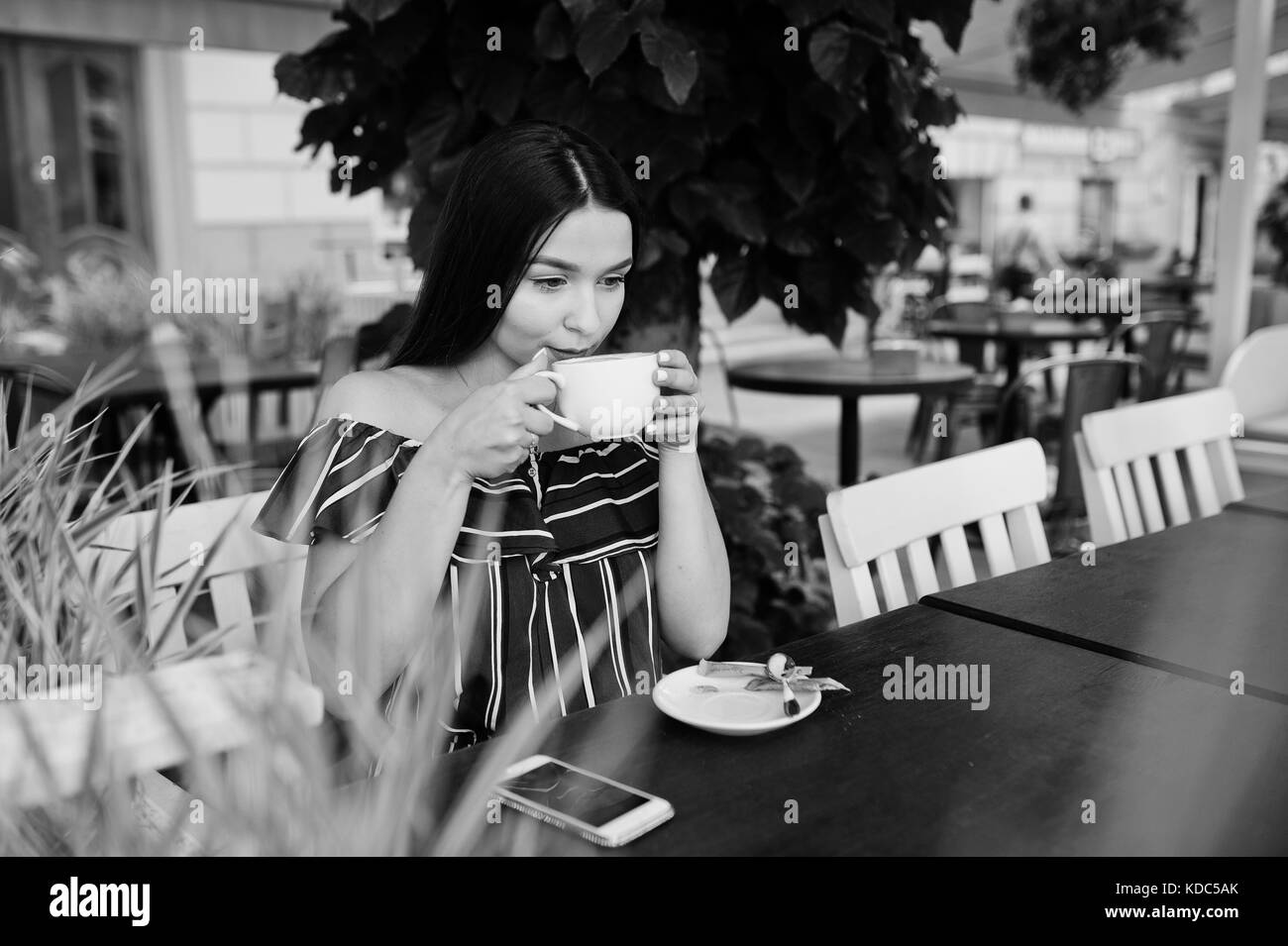 Gorgeous Brunette ragazza seduta sul tavolo in cafe con la tazza di caffè e bevande. Foto Stock