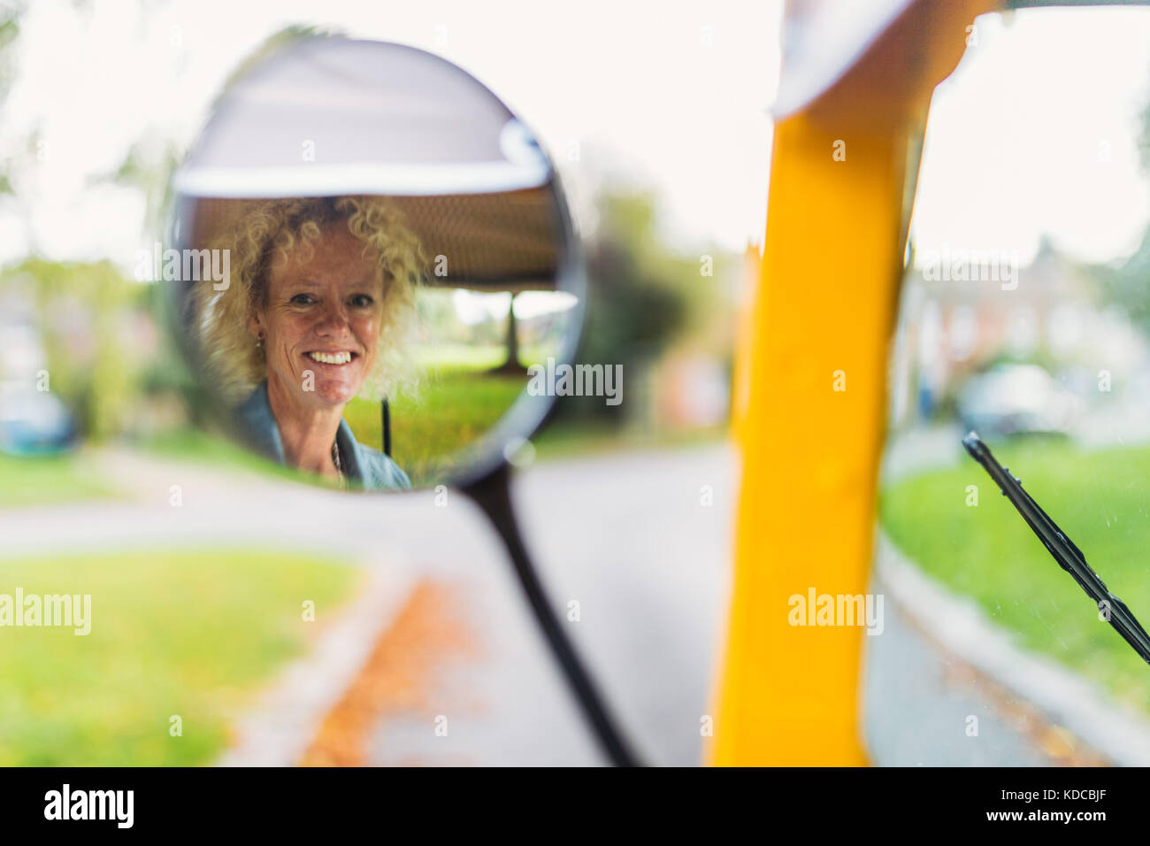 Una donna bionda visto nell'ala mirror come lei aziona un giallo tuk tuk in un villaggio inglese Foto Stock