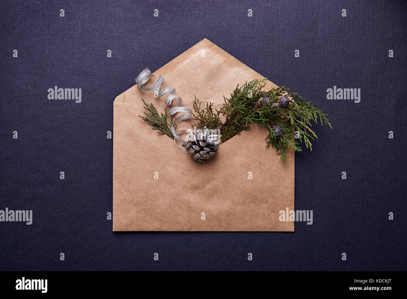 Decorazione per il natale. browm busta, evergreen ramoscello e cono di pino verniciato in argento su sfondo blu Foto Stock