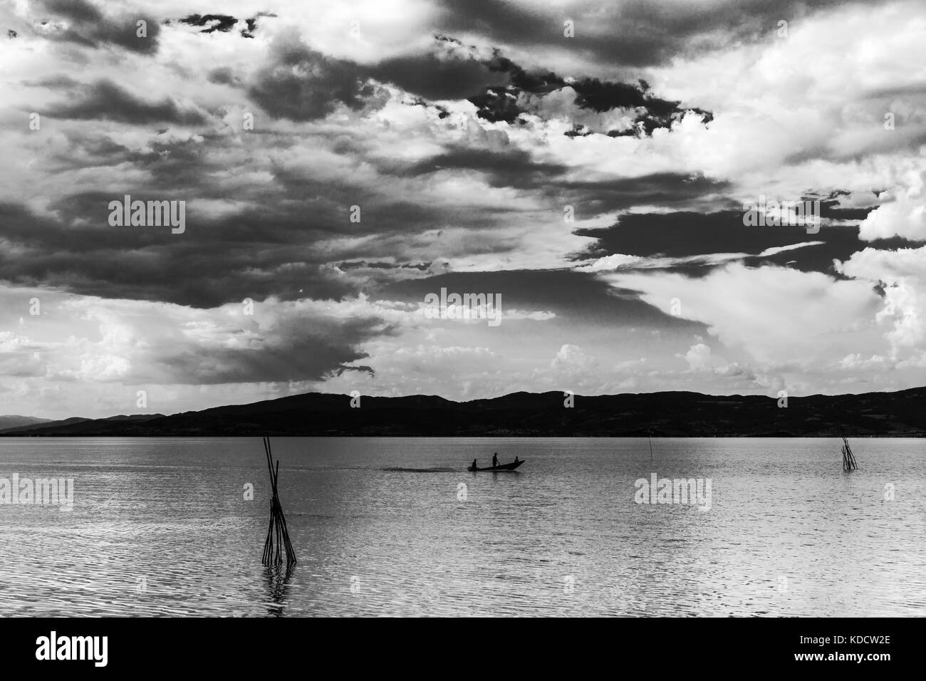 Una piccola barca con alcune persone su un lago, sotto una splendida, deep sky con nuvole bianche Foto Stock