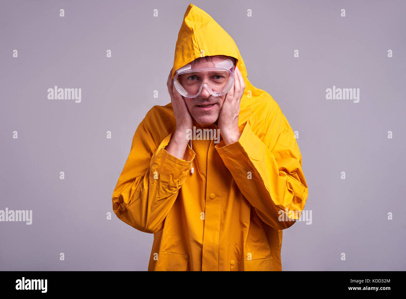 Un uomo di mezza età in un impermeabile giallo e occhiali di sicurezza spaventati Foto Stock