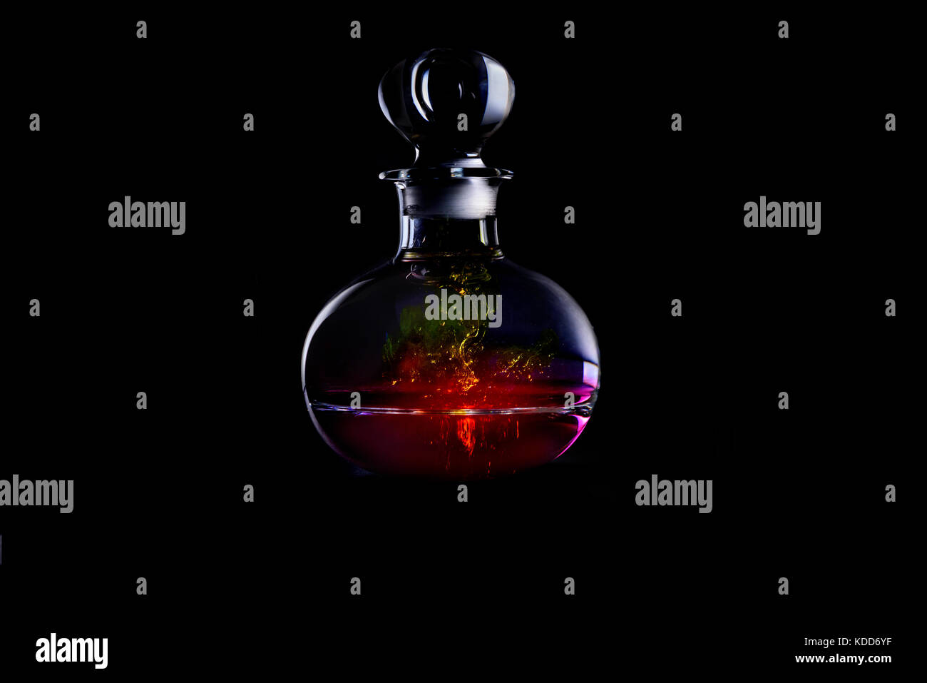 Decanter di vetro illuminato contenente acqua colorata con coloranti isolata contro uno sfondo nero Foto Stock