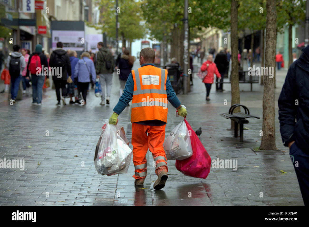 Uomo dello scomparto raccoglitore di rifiuti spazzatrice con sacchi della spazzatura a camminare sulla strada vista da dietro Foto Stock