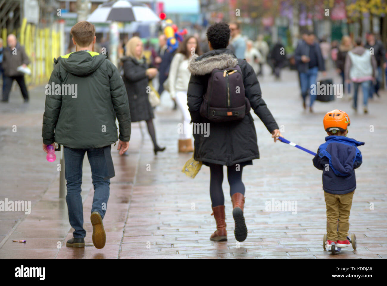 Famiglia giovane padre e madre trainare piccolo ragazzo su scooter visto da dietro a Buchanan Street lo stile di miglio Foto Stock