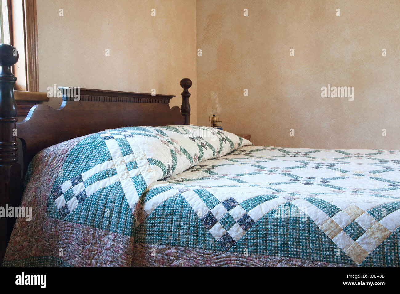 Un vecchio letto con una trapunta a fianco di una lampada ad olio Foto Stock
