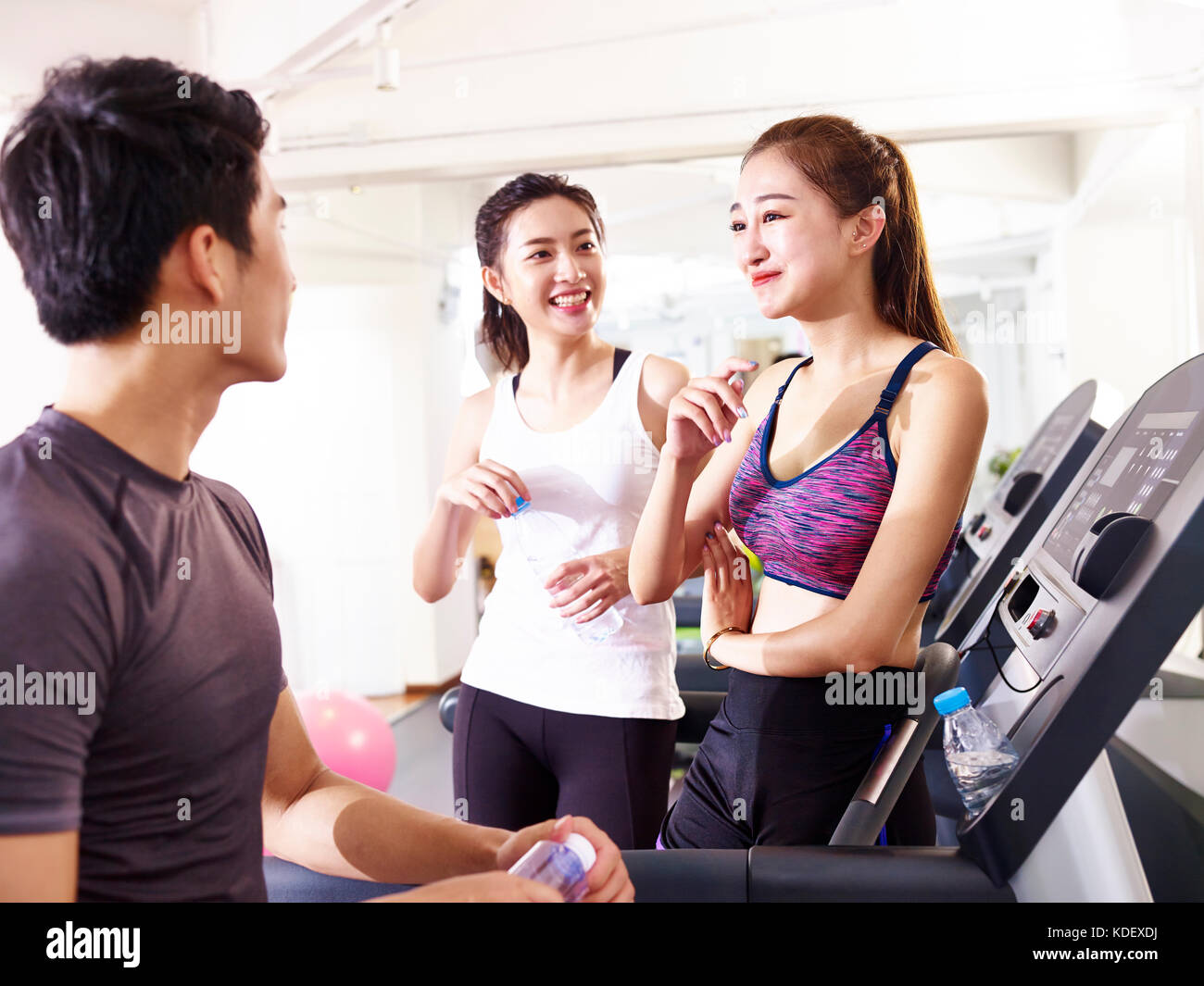 Giovane uomo asiatico e donne chiacchierando in palestra mentre prendendo una pausa. Foto Stock