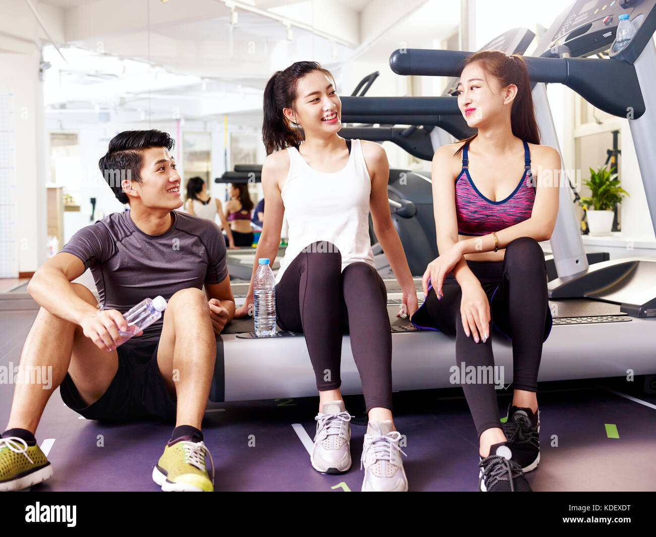 Giovane uomo asiatico e donne chiacchierando in palestra mentre prendendo una pausa. Foto Stock