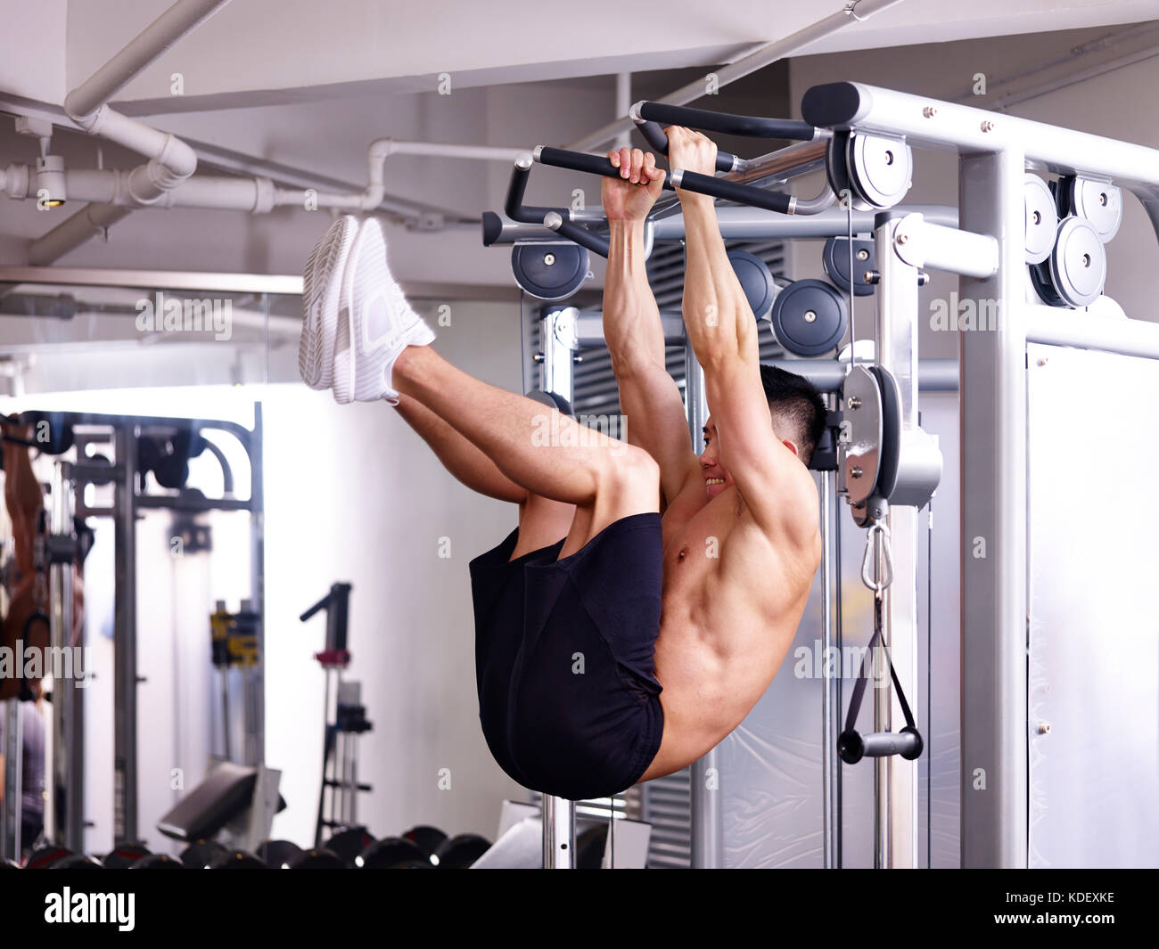 Asian bodybuilder esercitare la muscolatura addominale per impiccagione se stesso su apparecchiature. Foto Stock