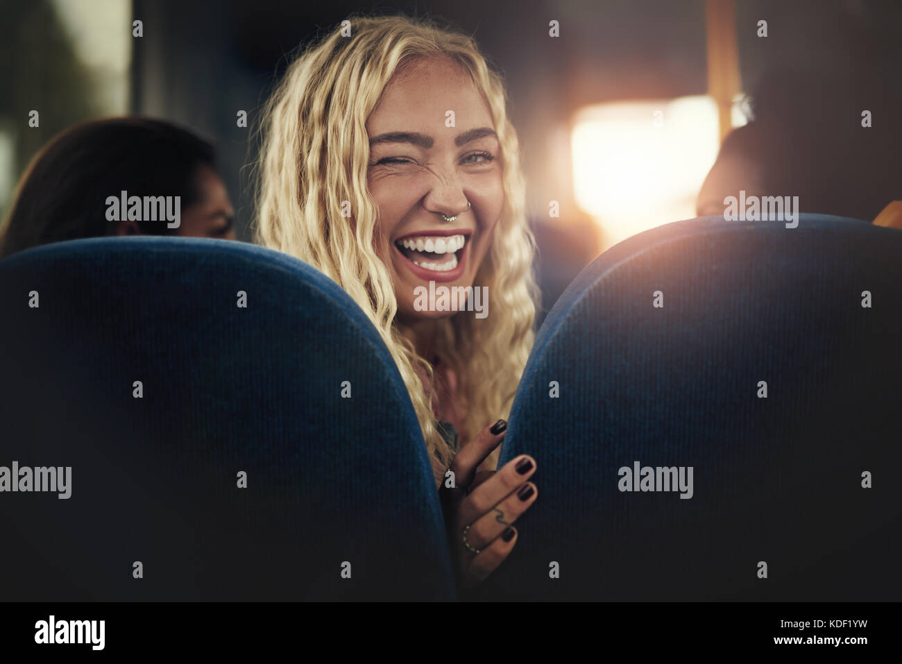 Ridendo bionda e giovane donna seduta da sola su un bus guardando sopra la sua spalla e occhiolino Foto Stock