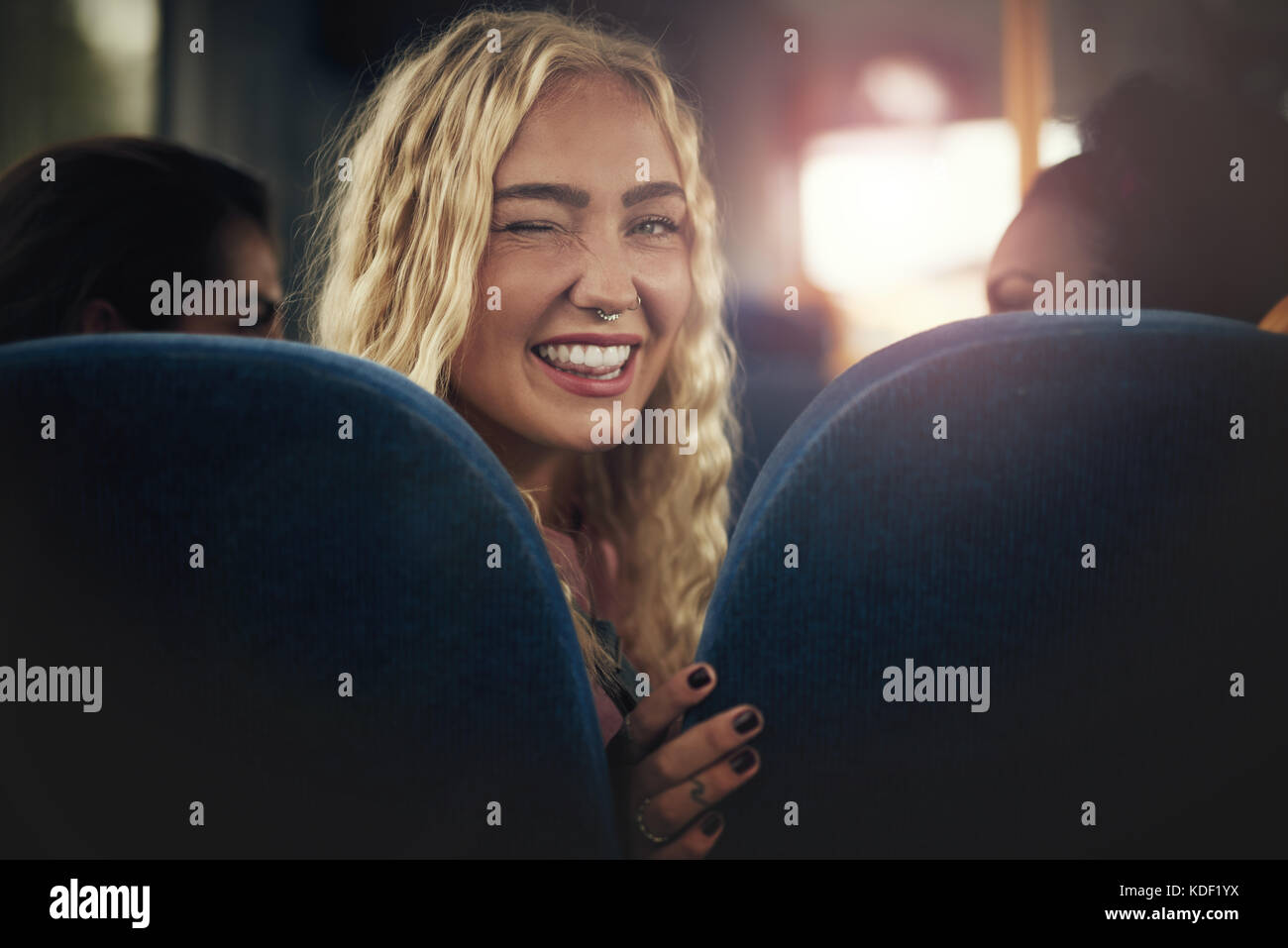 Sorridente bionda e giovane donna seduta su un bus guardando sopra la sua spalla e occhiolino Foto Stock