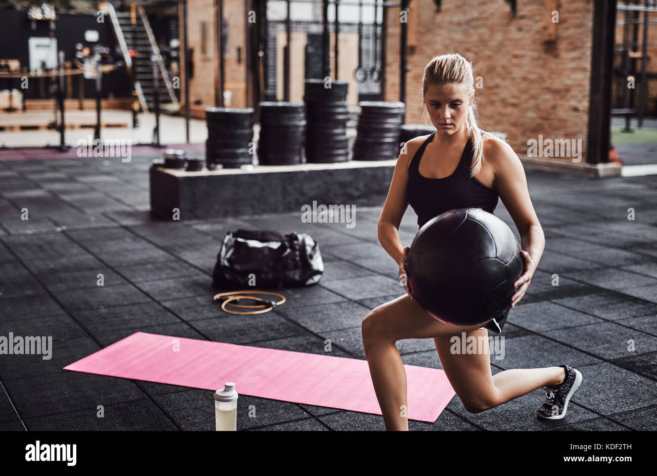 Montare la giovane donna bionda in sportswear facendo esercizi di nucleo con una palla ginnica mentre si lavora fuori da solo in una palestra Foto Stock
