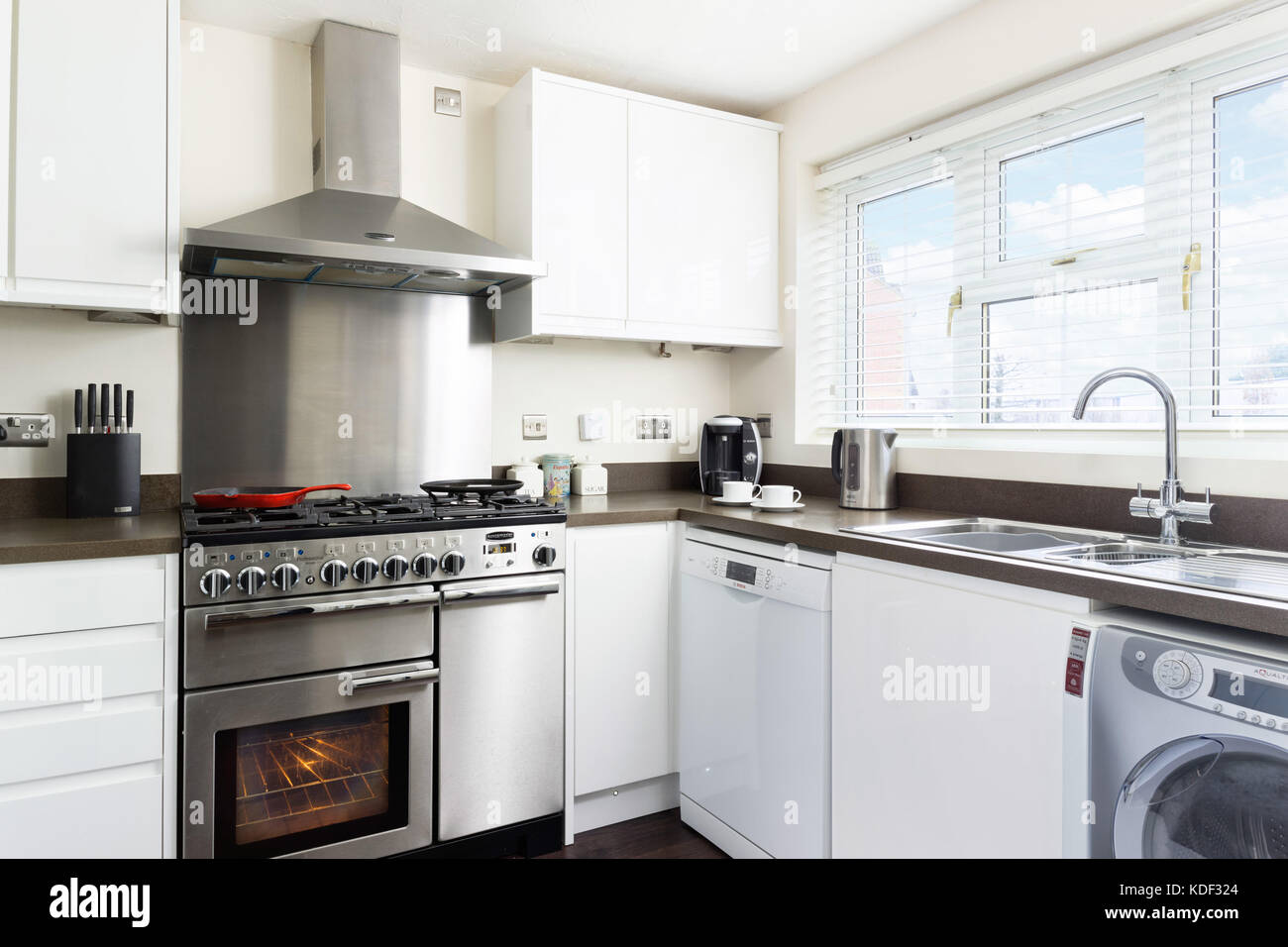 Una cucina piccola, pulita, fresca e bianca con fornello in acciaio inox, schiena e cappuccio in una tipica casa britannica moderna. Foto Stock