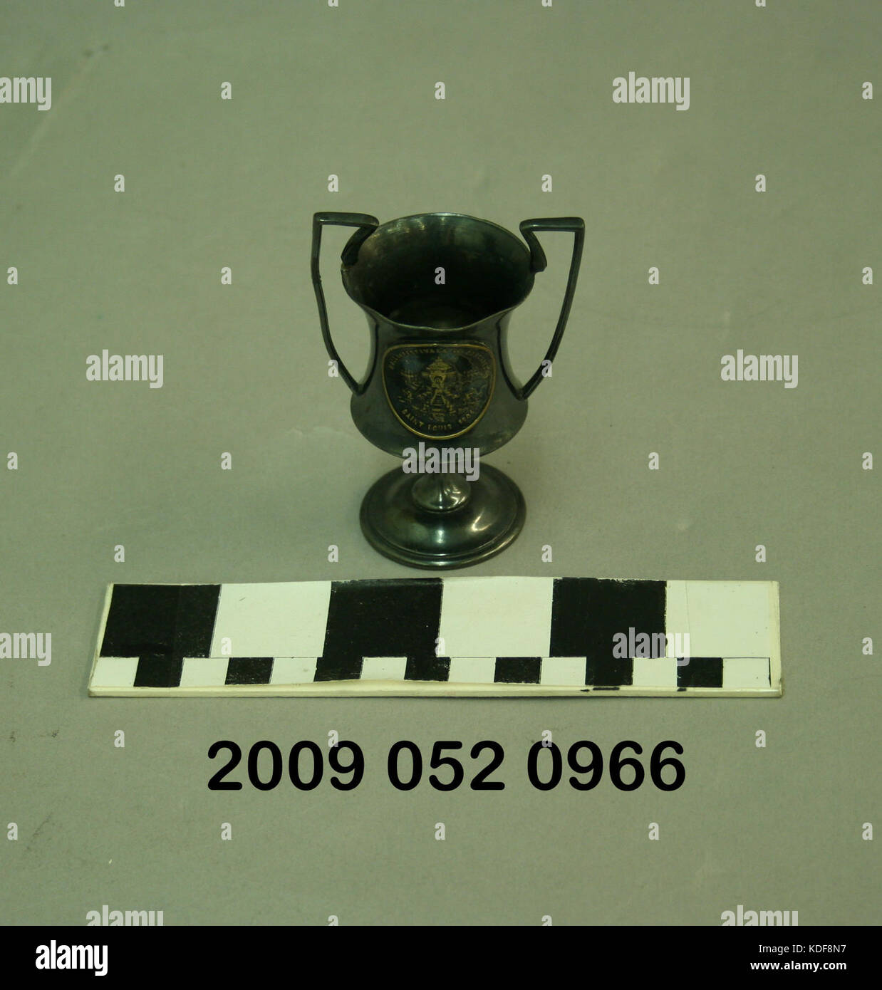 Un piccolo trofeo di metallo con un'immagine in rilievo della Festival Hall e degli elementi a cascata. Questo trofeo simboleggia un evento o un risultato specifico, con intricati dettagli di design che riflettono le caratteristiche architettoniche della sala e l'ambiente naturale circostante. Foto Stock