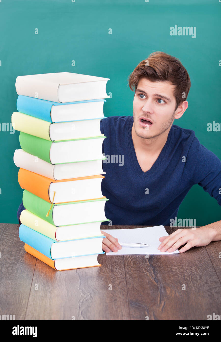 Ritratto di un maschio scioccato studente guardando alla pila di libri Foto Stock