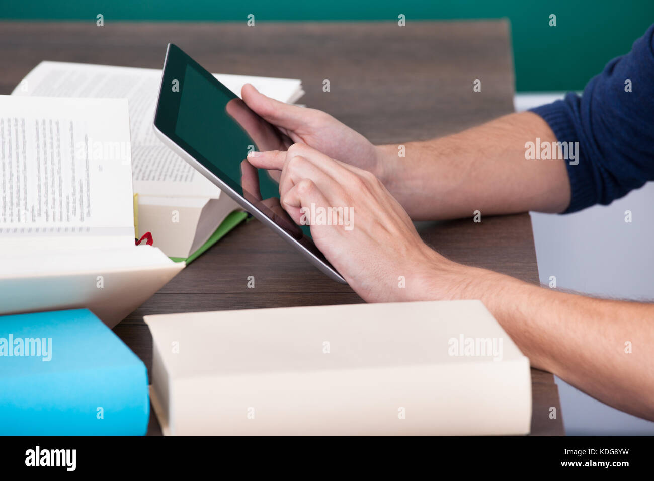 Studente maschio circondato da libri utilizzando tavoletta digitale Foto Stock