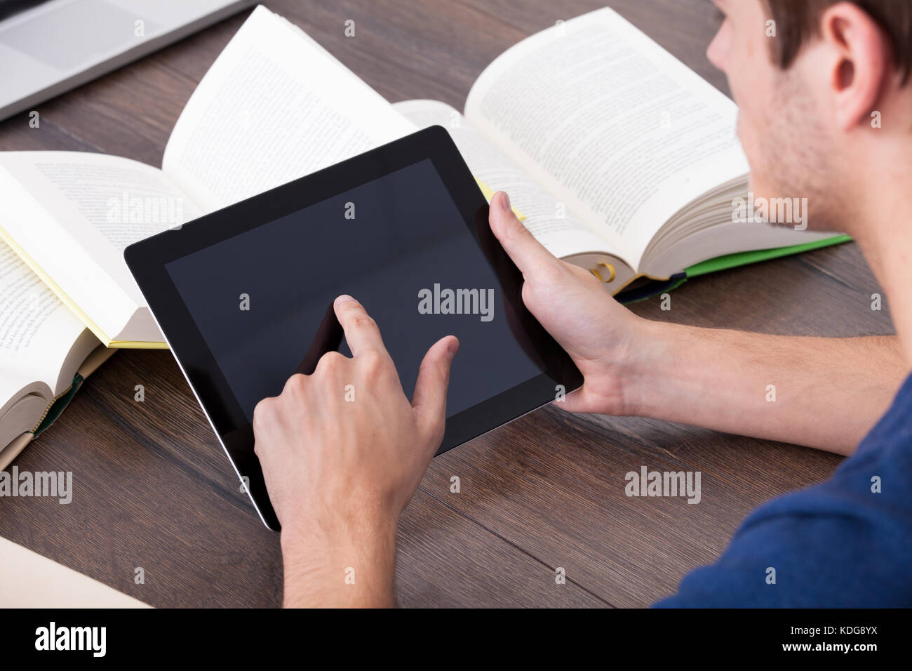 Studente maschio circondato da libri utilizzando tavoletta digitale Foto Stock