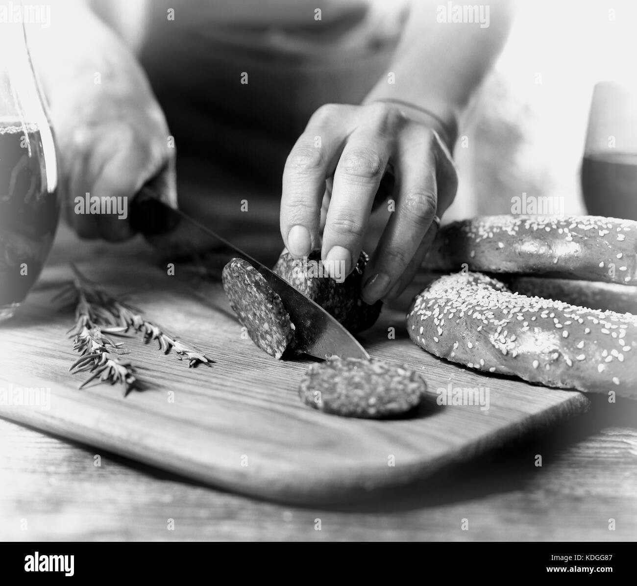 Foto in bianco e nero tradizionale italiano vino rosso, salame, rosmarino, pane. stretta di mano di una persona salame tagliato su una cucina scheda effetto filmato Foto Stock