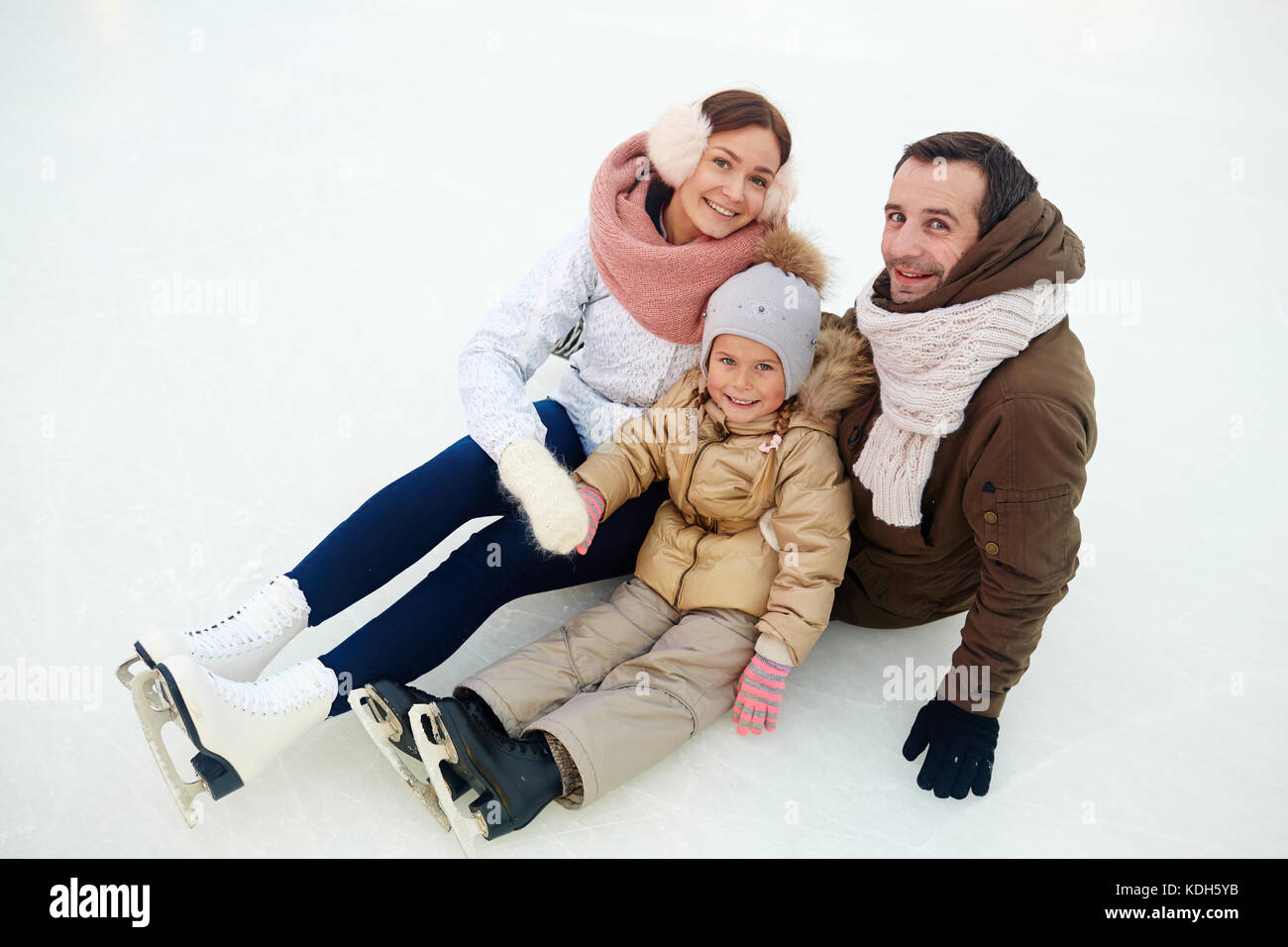 Allegro famiglia del padre, madre e figlia piccola in activewear e pattini seduti sulla neve Foto Stock