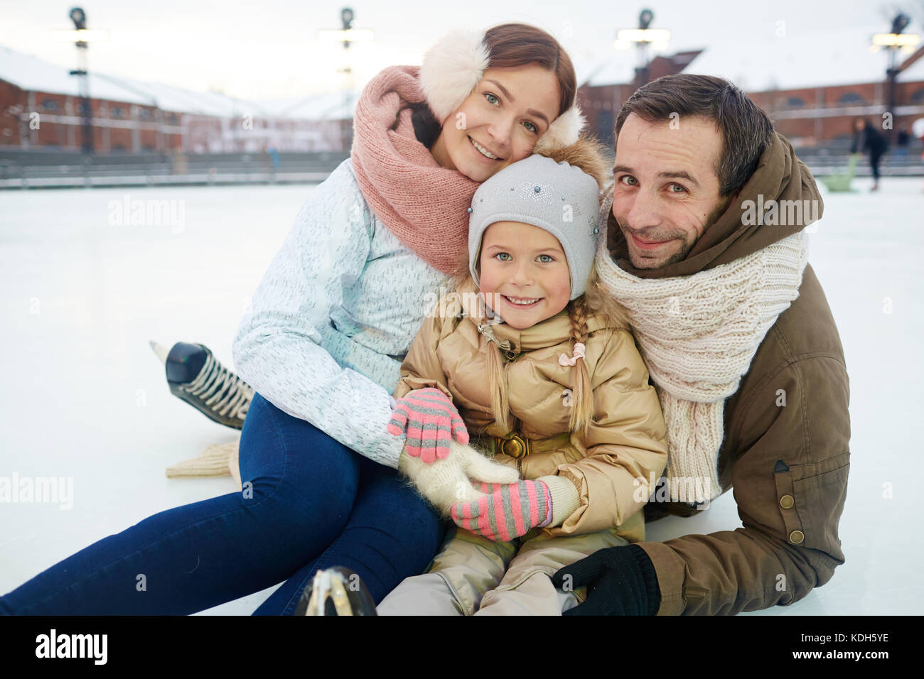 Affettuosa e famiglia attiva in winterwear seduti sulla pista di pattinaggio Foto Stock