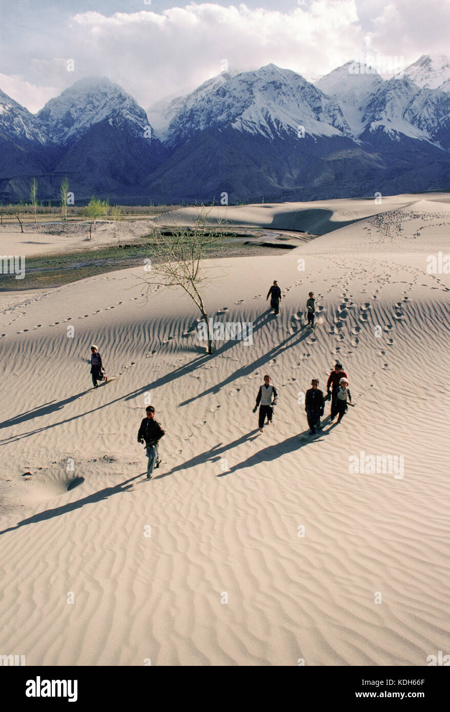 I ragazzi di ritorno da scuola attraverso le dune di sabbia in Skardu, la parte superiore della valle di Indus, Kashmir Pakistan, 1990. Foto Stock
