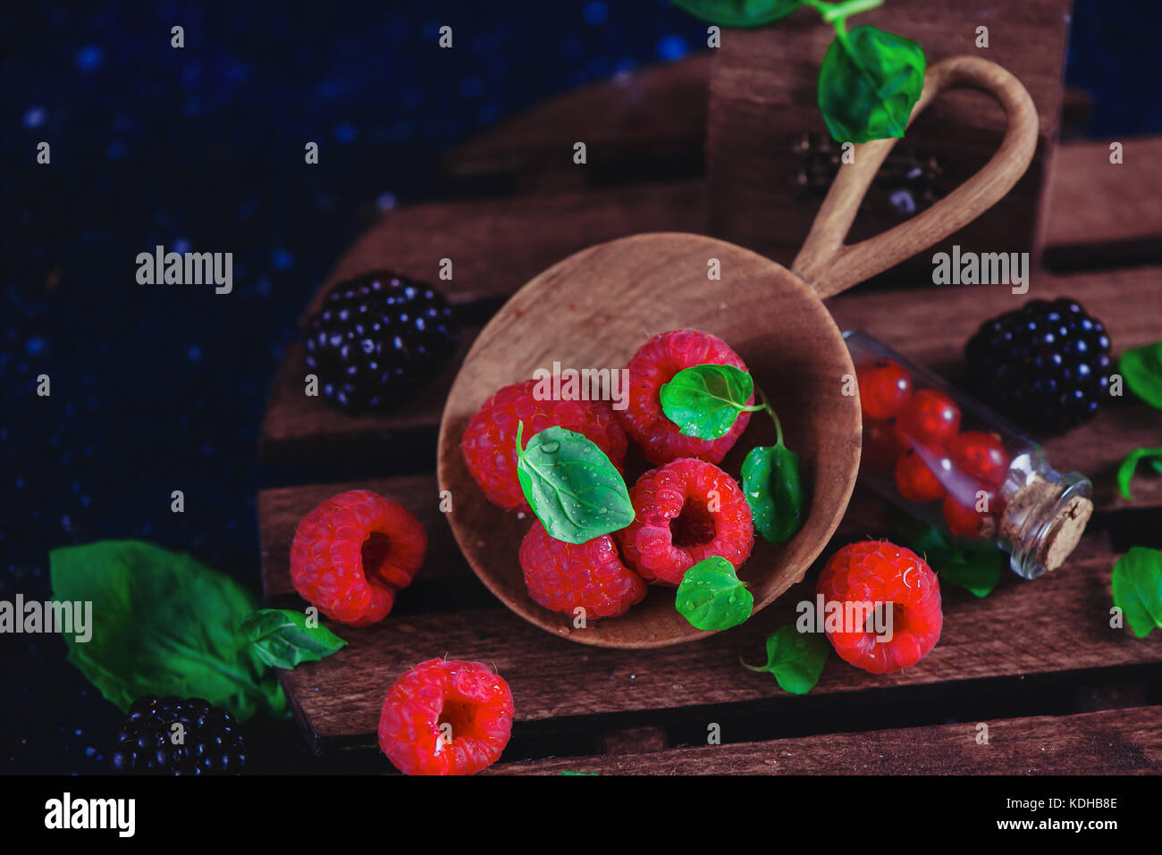 Frutti di bosco assortiti in una serva piatto di legno. lampone e blackberry con verde menta foglie scure della fotografia di cibo con copia spazio. Foto Stock